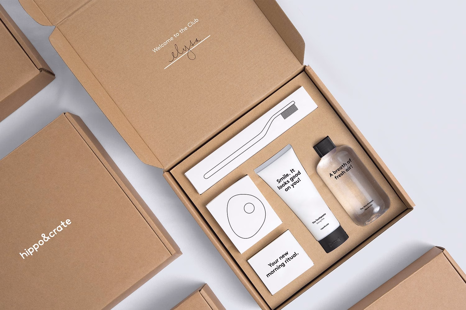 A brown cardboard box displays a toothbrush, a tube of cream, and cards with minimalist black typography.
