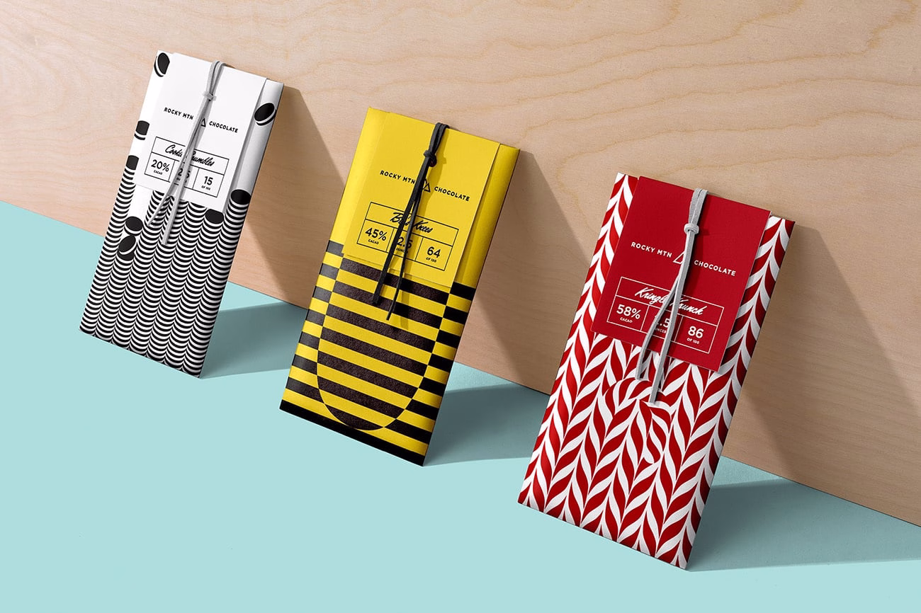 Three chocolate bars with distinct patterns—black and white waves, yellow stripes, and red leaves—are displayed on a light blue surface.