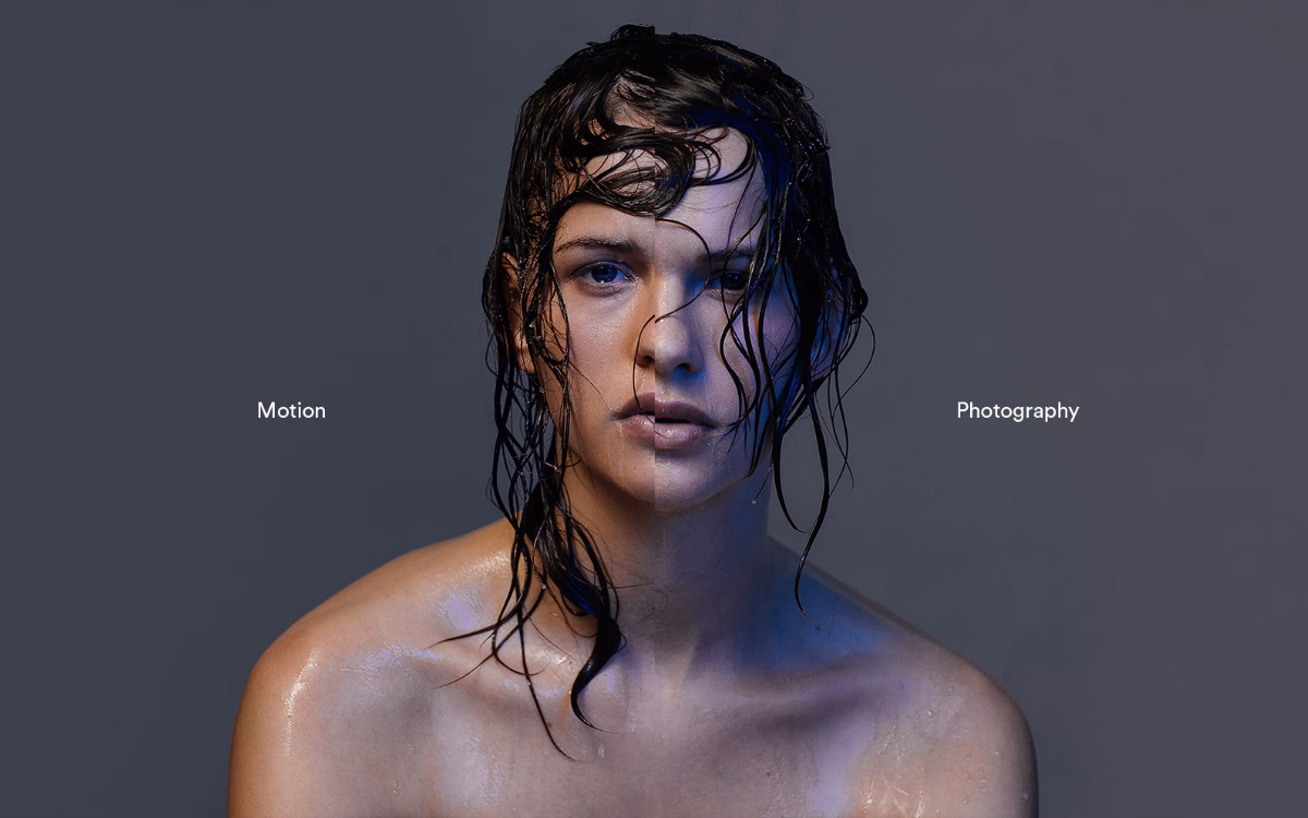 A close-up of a person with wet hair, gazing directly at the camera, against a softly lit gray background.