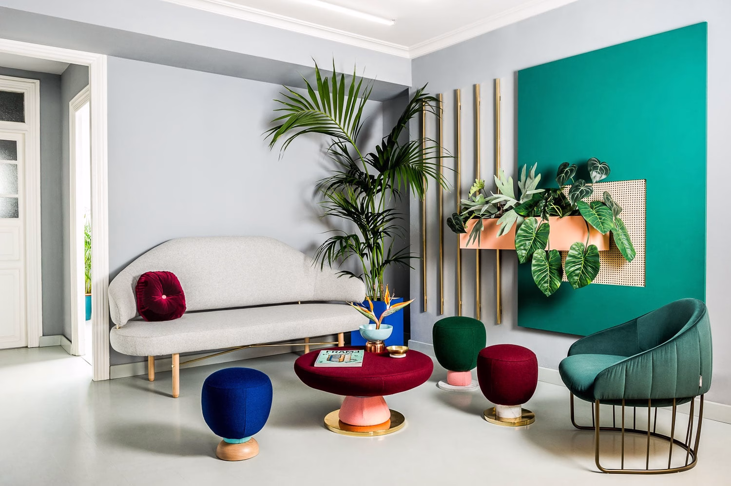A modern living room featuring a gray sofa, colorful stools, and a green accent wall with plants and gold accents.