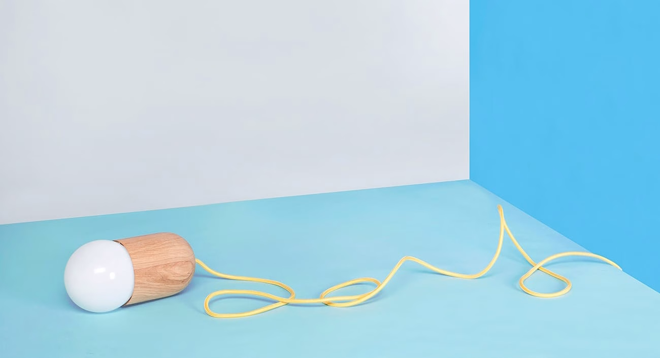 A wooden lamp with a white globe sits on a light blue surface, its yellow cord curving around it.