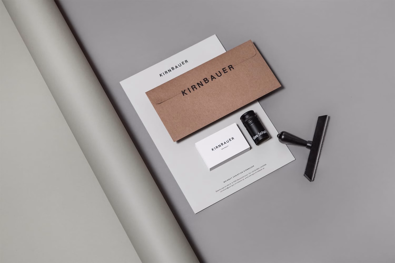 A minimal arrangement of stationery items on a grey surface, featuring a brown envelope and a black stamping tool.