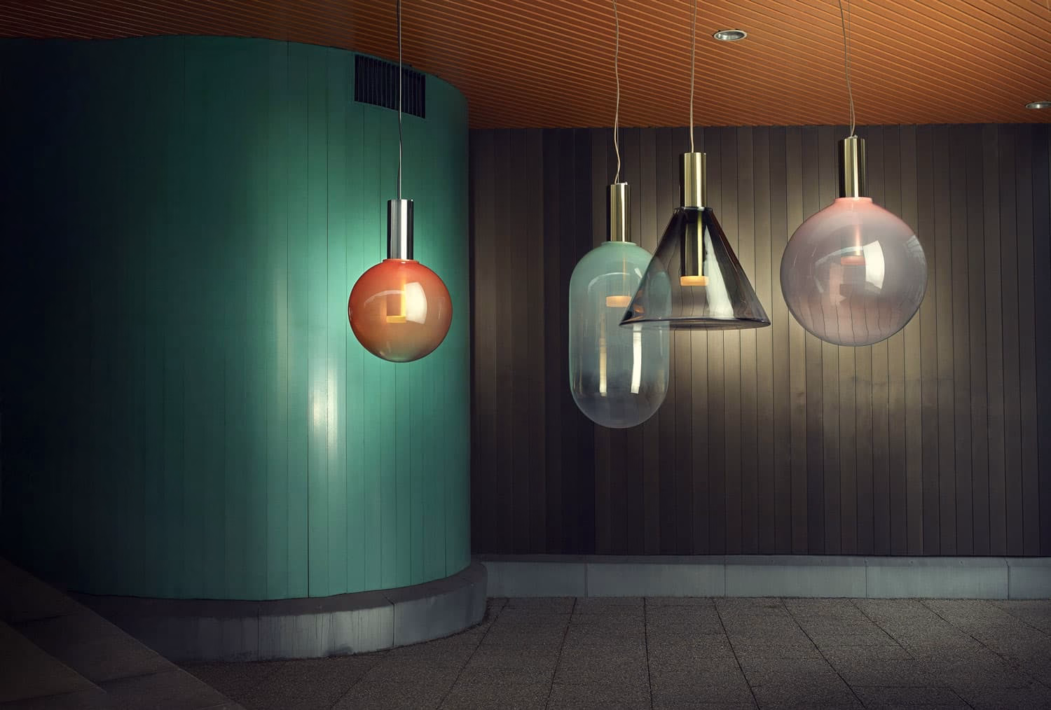 Four hanging lamps in various shapes and colors illuminate a textured wall with a green column and wooden ceiling.