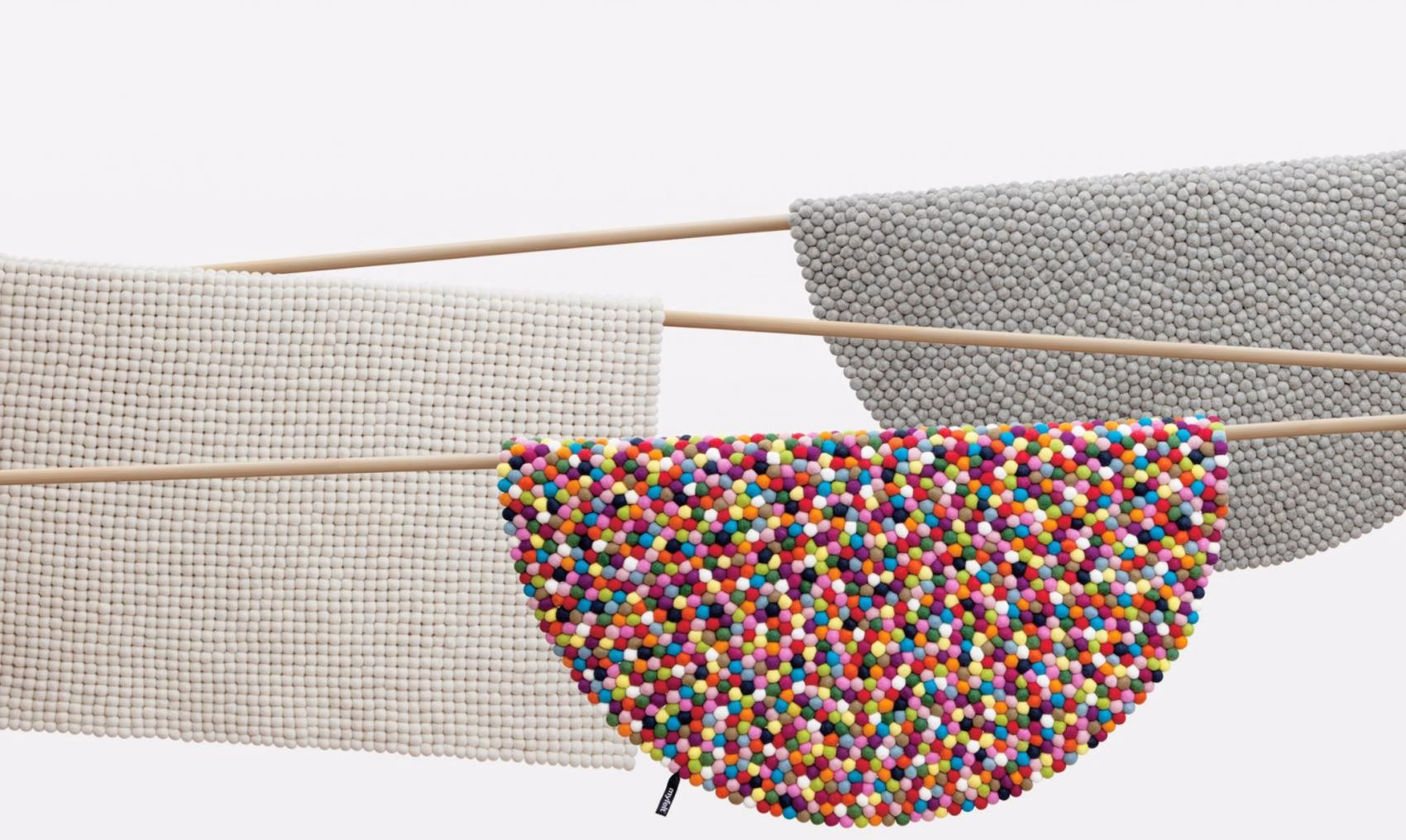 Three textured fabric panels hang from wooden rods, featuring a colorful design, gray, and white tones.