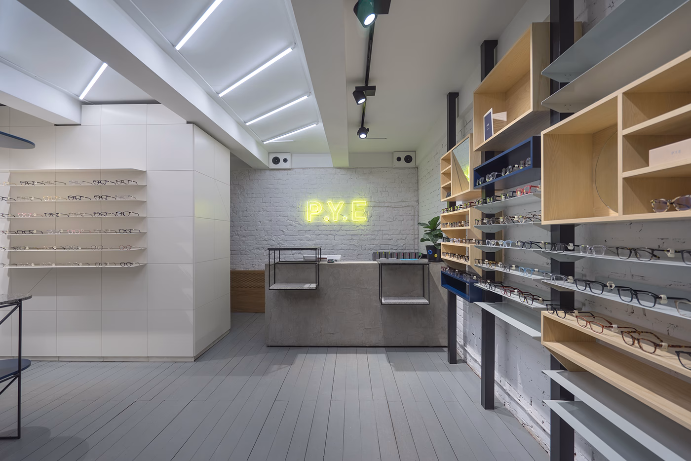 A modern eyewear store features sleek wooden shelves and a neon sign against a white brick wall.