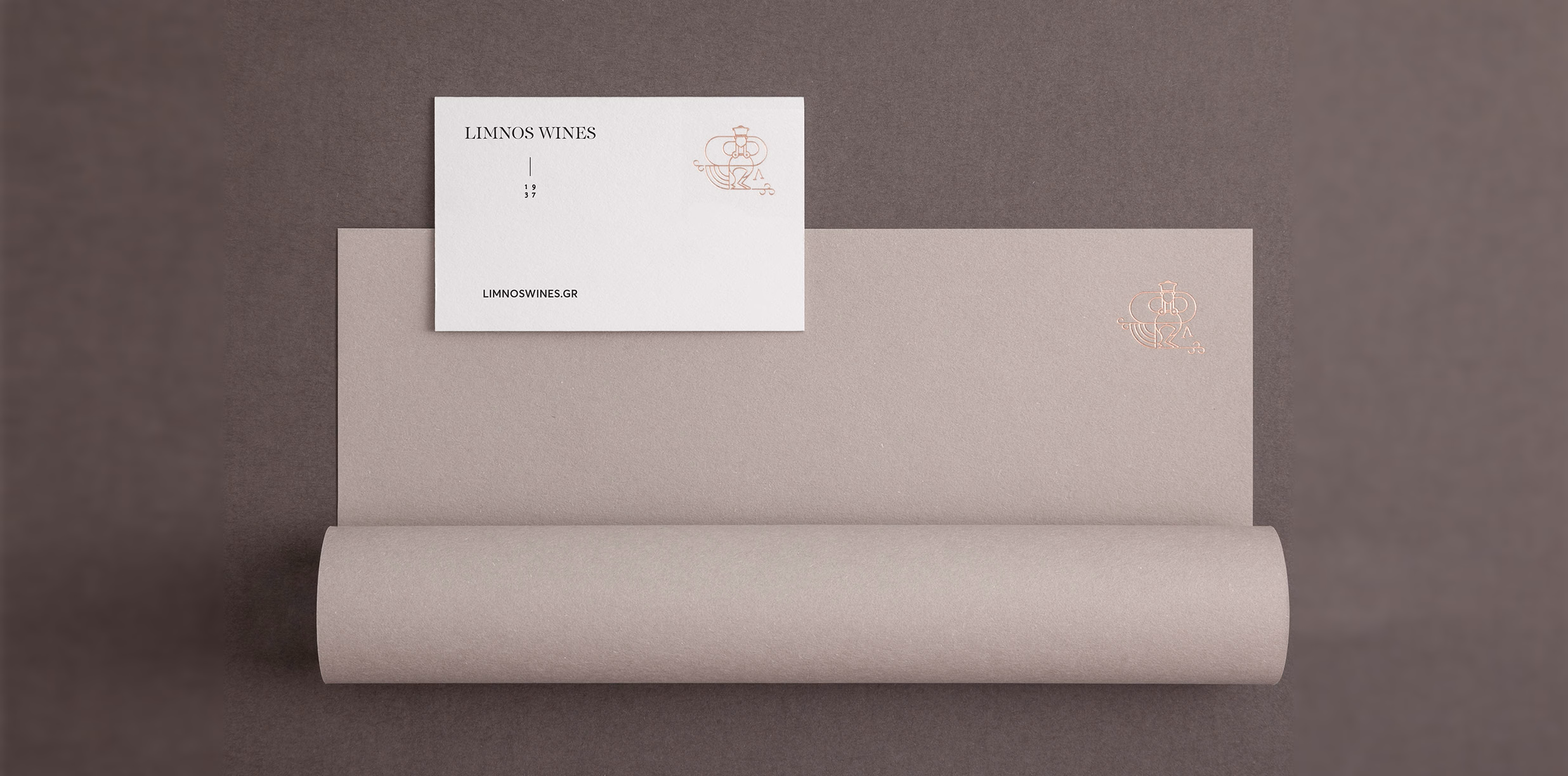 A minimalist design featuring a white business card atop textured gray paper, with subtle copper detailing.