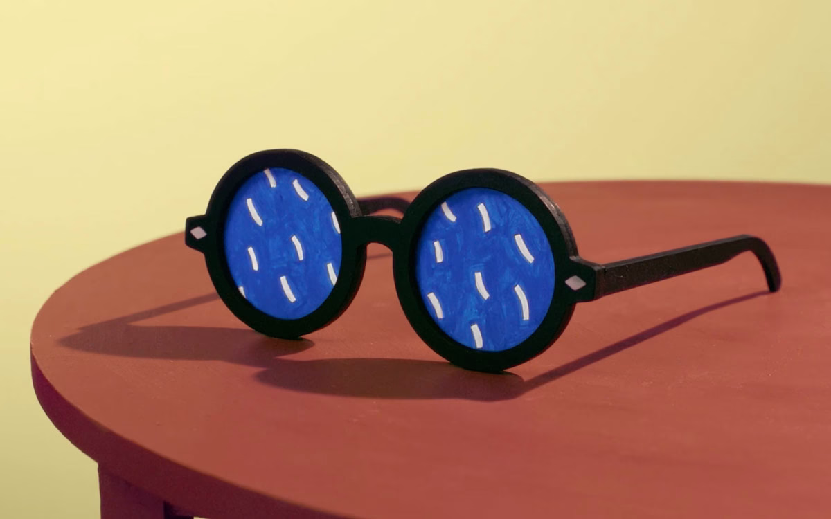 Black sunglasses with blue lenses featuring white designs, resting on a round reddish table against a yellow background.