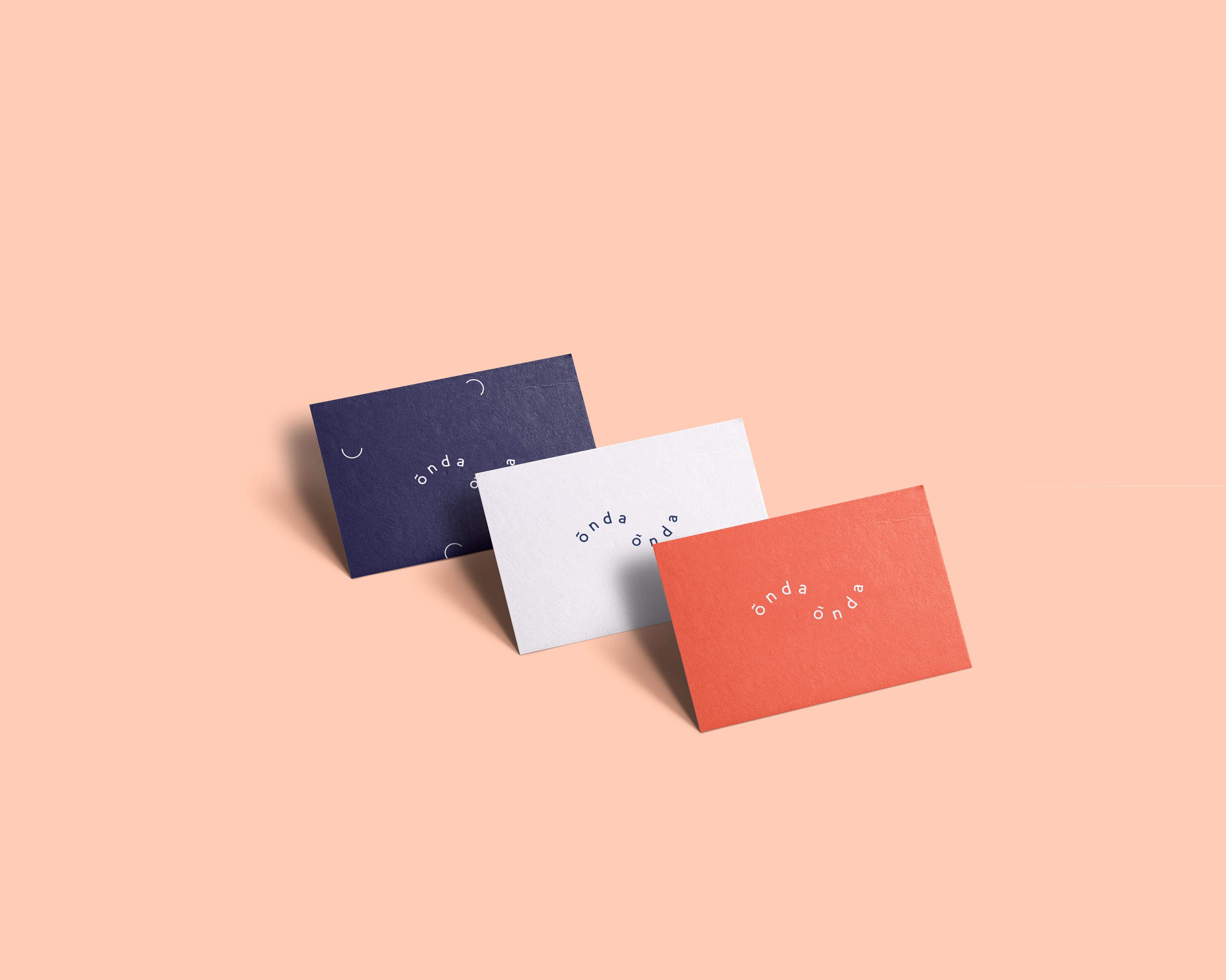 Three business cards in navy, white, and coral are arranged on a soft peach background, showcasing minimal typography.
