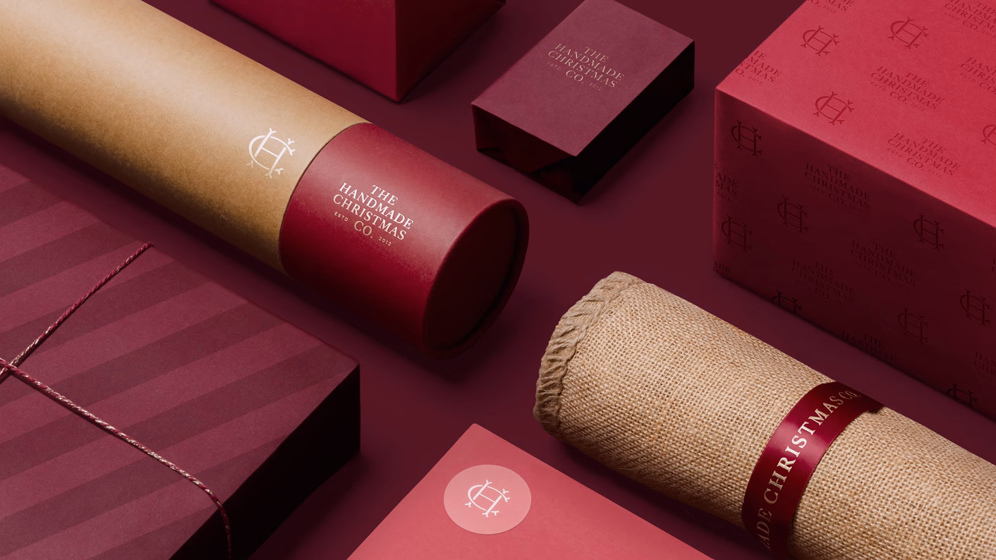 A selection of festive packaging in rich red and brown tones includes boxes, wrapping, and a burlap tube.