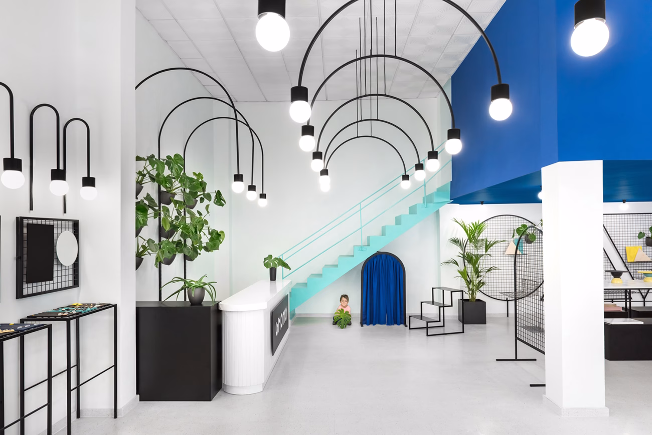 A bright, modern space features curved black pendant lights and a blue accent wall, with a child near green plants.