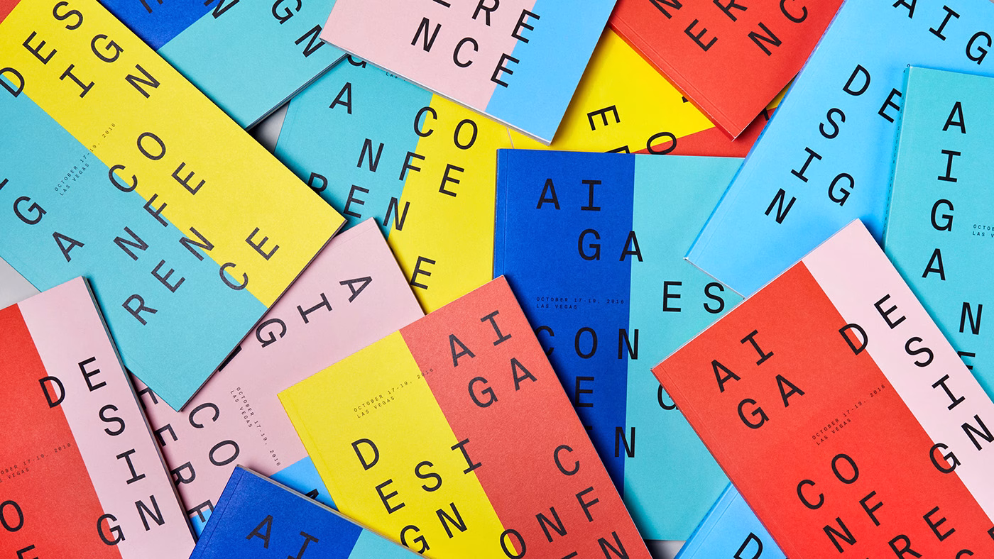 A scattered collection of colorful conference brochures features bold black typography against vibrant backgrounds.