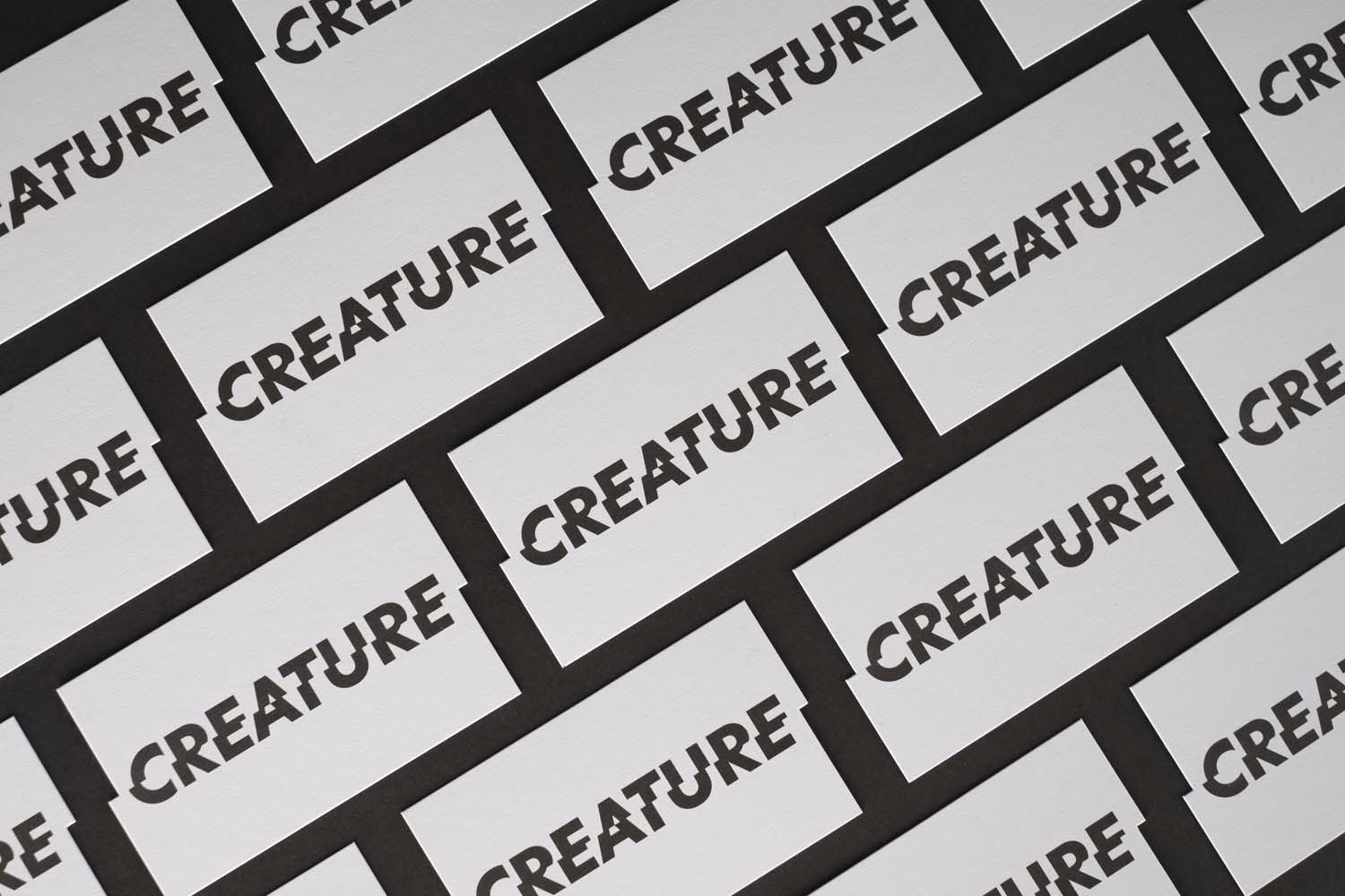 A pattern of overlapping white cards featuring bold black text reading "CREATURE" against a dark background.