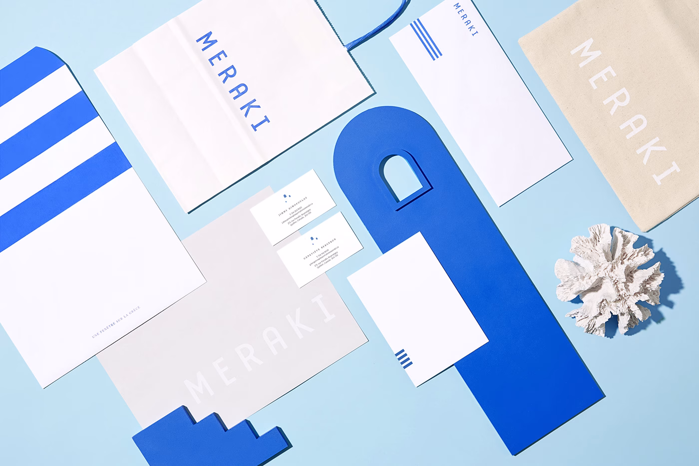 A flat lay of branding materials in blue and white, featuring a coral piece and various stationery items.