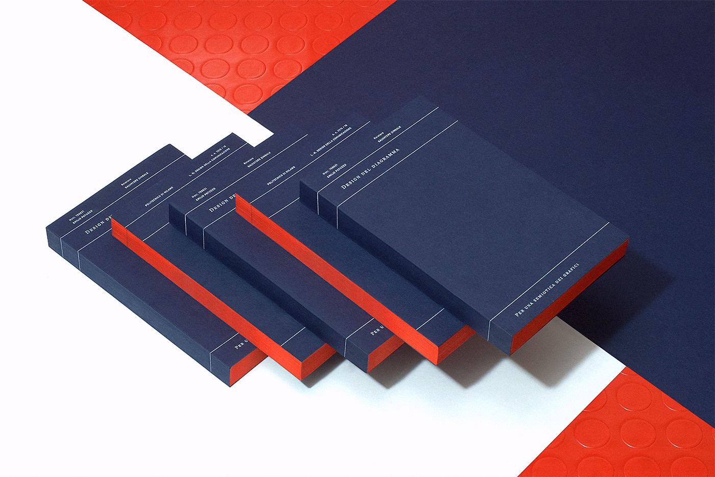 A series of navy blue booklets with red spines arranged on a textured red and white surface.
