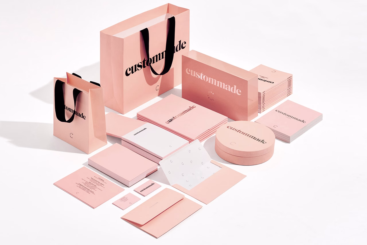 A collection of pink paper goods and bags with bold black typography, arranged on a light surface.
