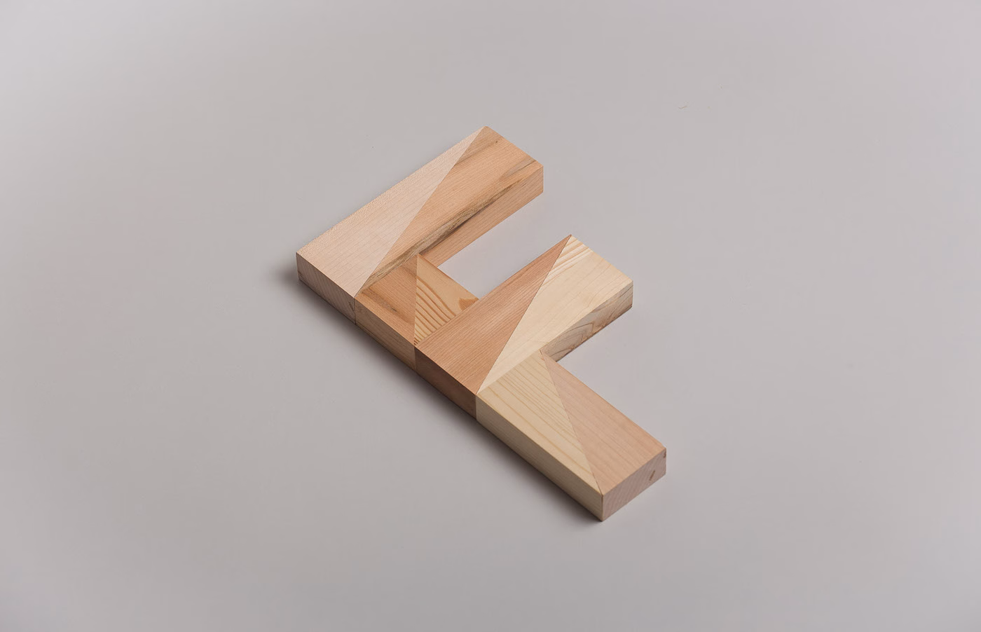 A geometric wooden object with angled surfaces, featuring light natural hues, rests on a gray background.