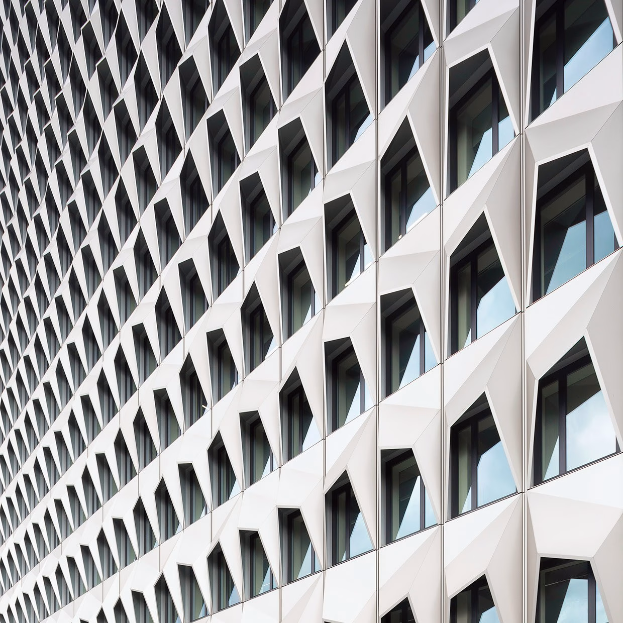 A geometric façade features a pattern of protruding diamond shapes and sleek windows reflecting the sky.
