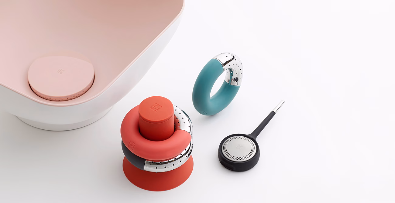 A collection of modern kitchenware in soft pink, coral, and teal, arranged on a white surface.