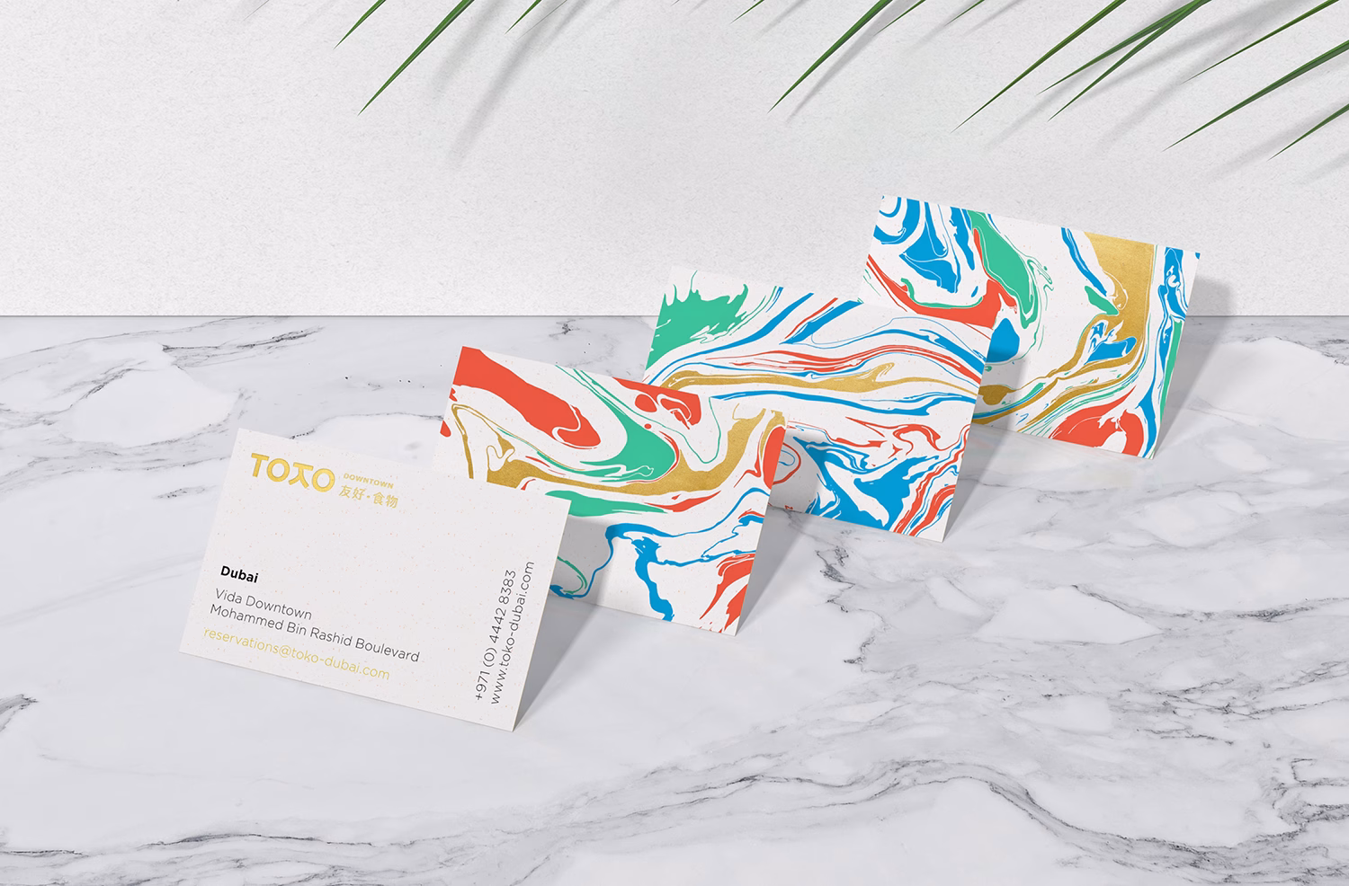 Three marbled business cards in vibrant colors are arranged on a marble surface, next to a contact card.