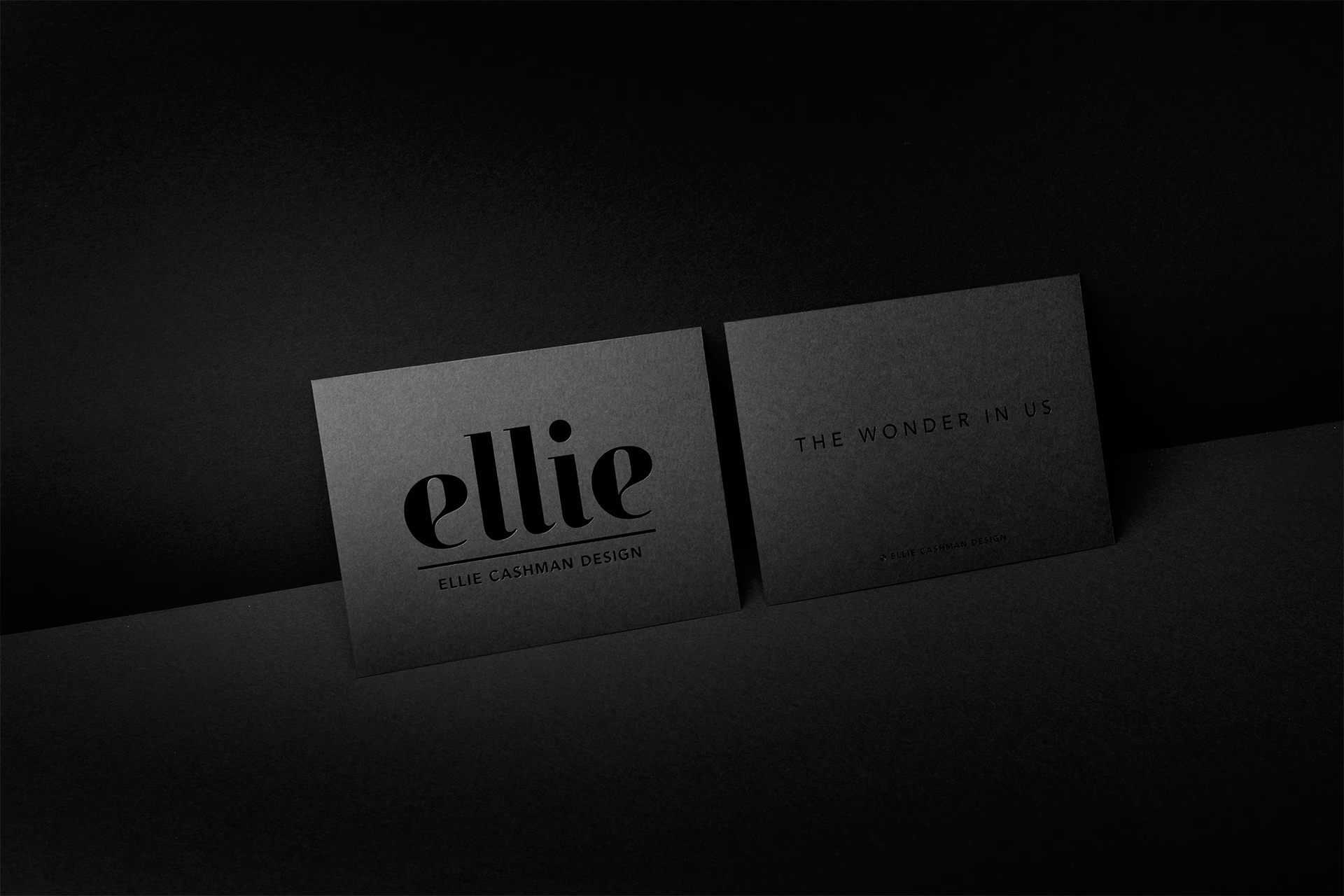 Two sleek black business cards sit on a dark surface, featuring bold typography against a minimal backdrop.