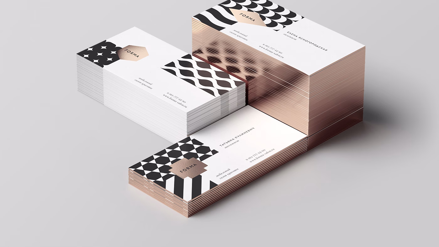 A stack of business cards features black geometric patterns on white with a rose gold edge, displayed on a gray surface.
