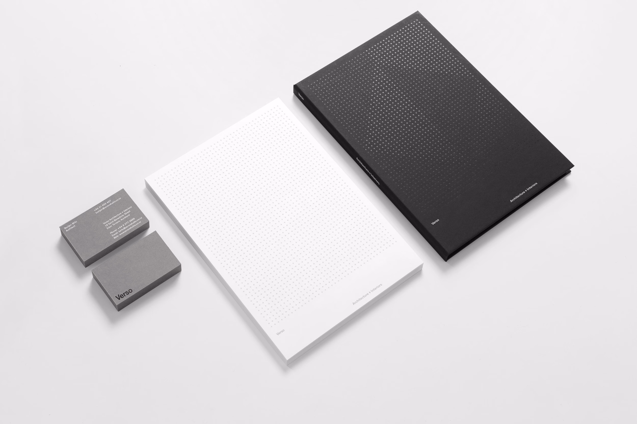 A black notebook with a dotted design, a white dotted pad, and two gray business cards arranged on a white surface.