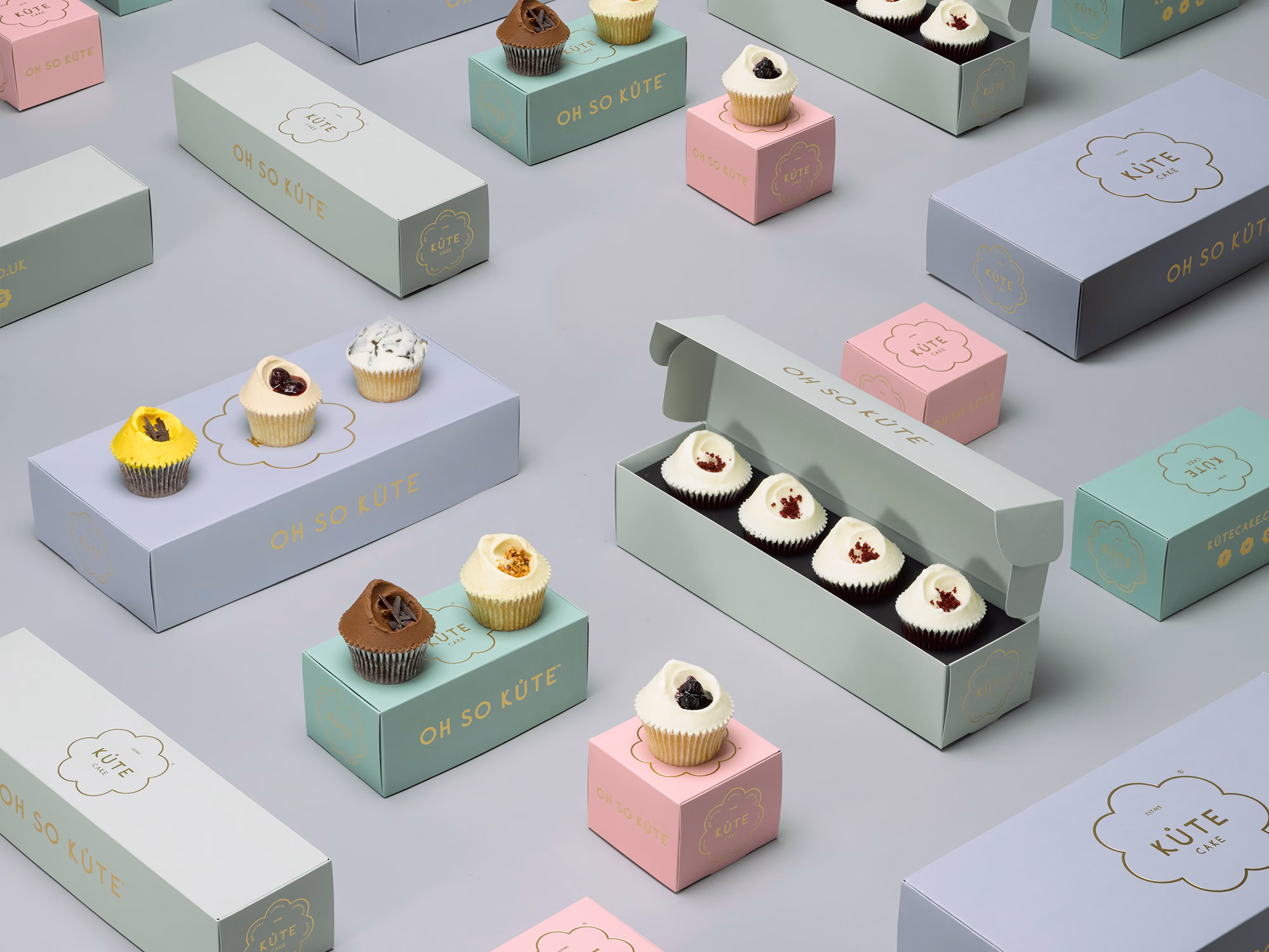 A collection of pastel-colored cupcake boxes arranged on a grey surface, showcasing decorative cupcakes atop them.