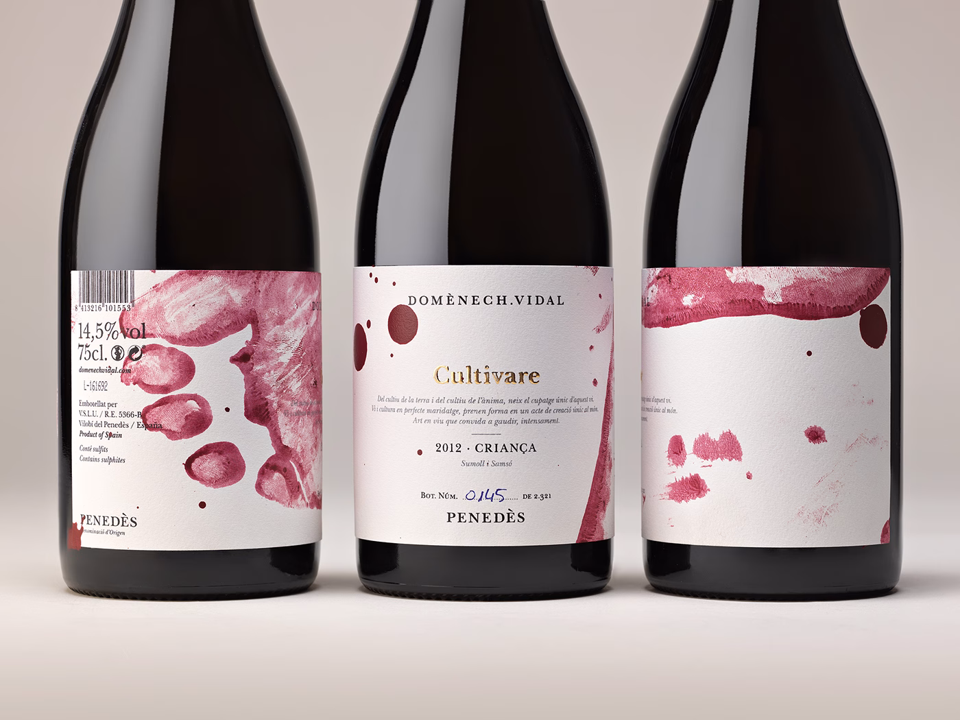 Three wine bottles with textured labels featuring red splashes and a minimalist design, showcasing artisanal craftsmanship.