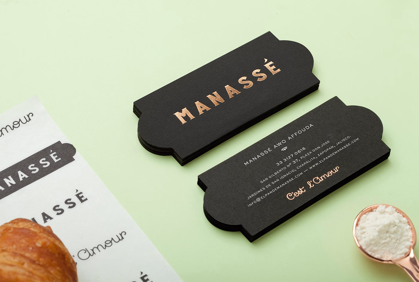 A black card with copper lettering displays "MANASSÉ" alongside a croissant and a spoonful of flour on a mint background.