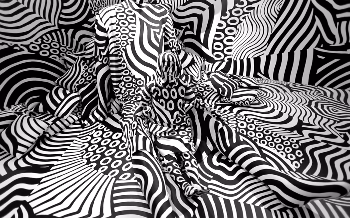 A wrinkled fabric displays bold black and white patterns of swirling lines and circles, creating a dynamic visual texture.