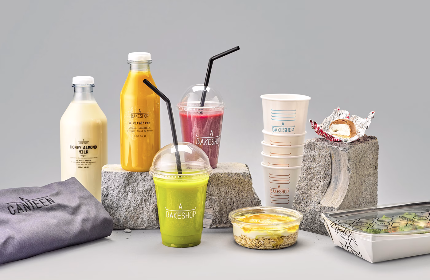 A collection of drinks and food items on concrete blocks, featuring a green smoothie and colorful juice bottles.