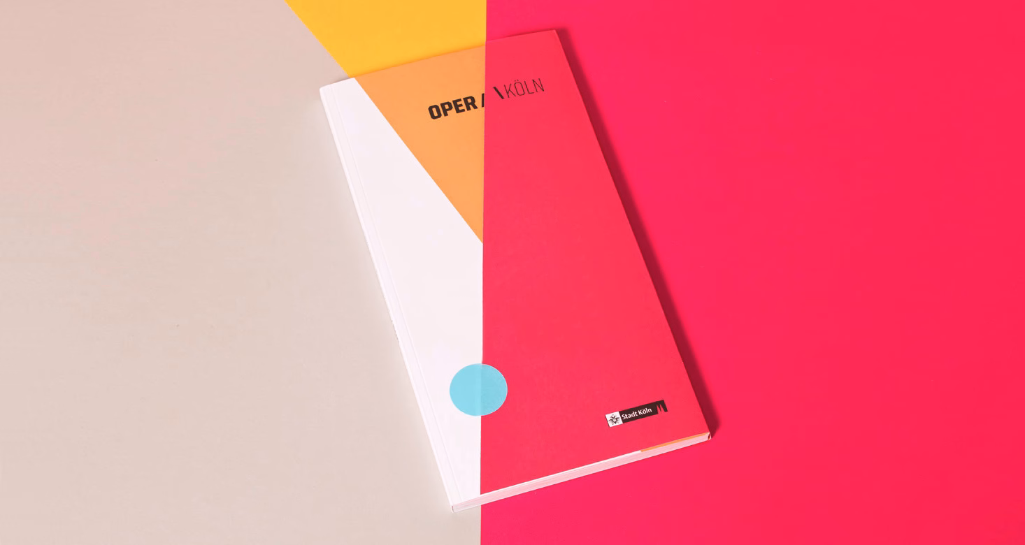 A vibrant pink and orange booklet is displayed against a neutral background, featuring geometric shapes and bold typography.