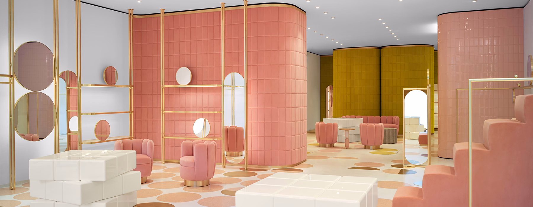 A brightly colored interior features pink and yellow walls, round mirrors, and plush seating arranged around light-hued flooring.