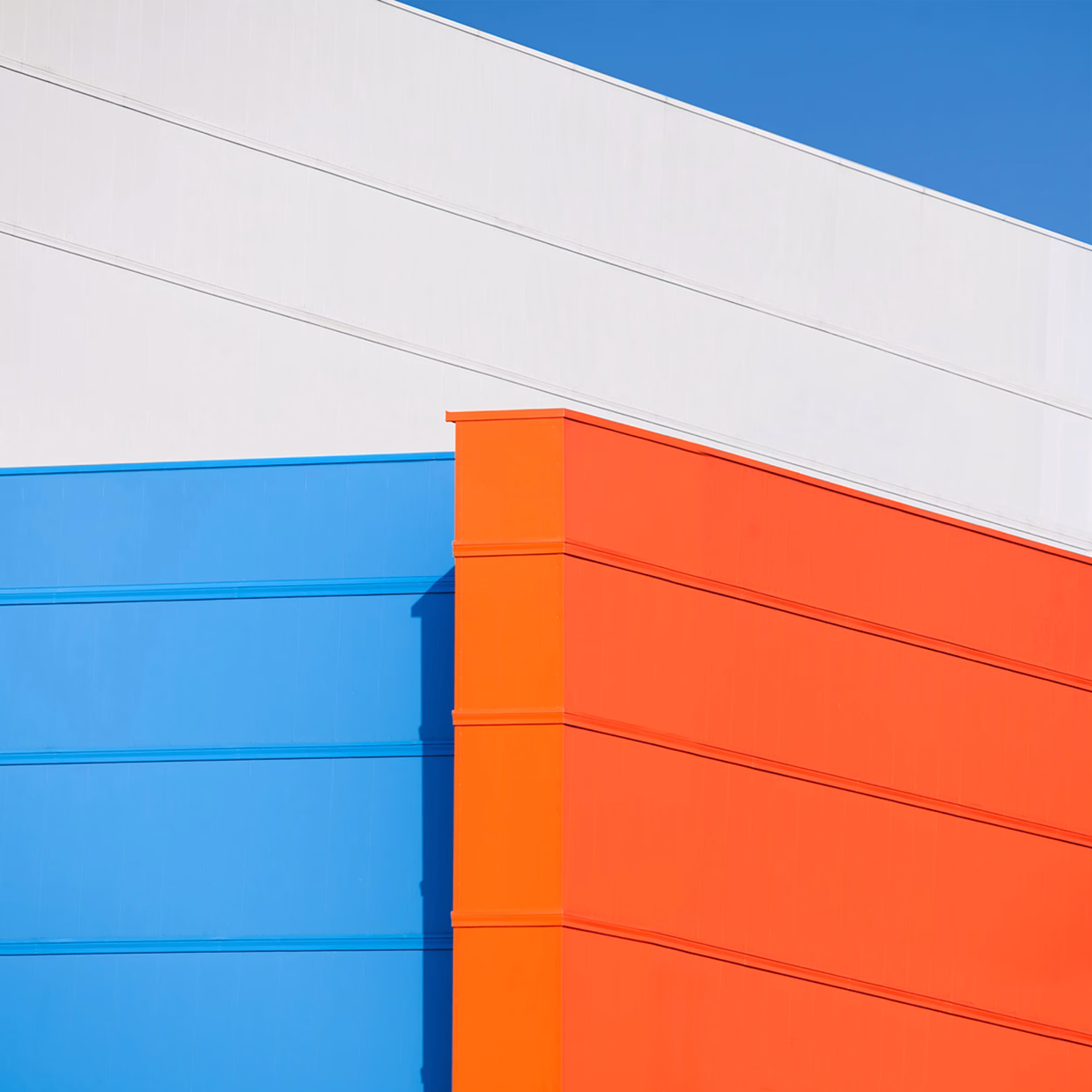 A section of a building features vibrant blue and orange panels against a clear blue sky, with clean lines and a modern design.