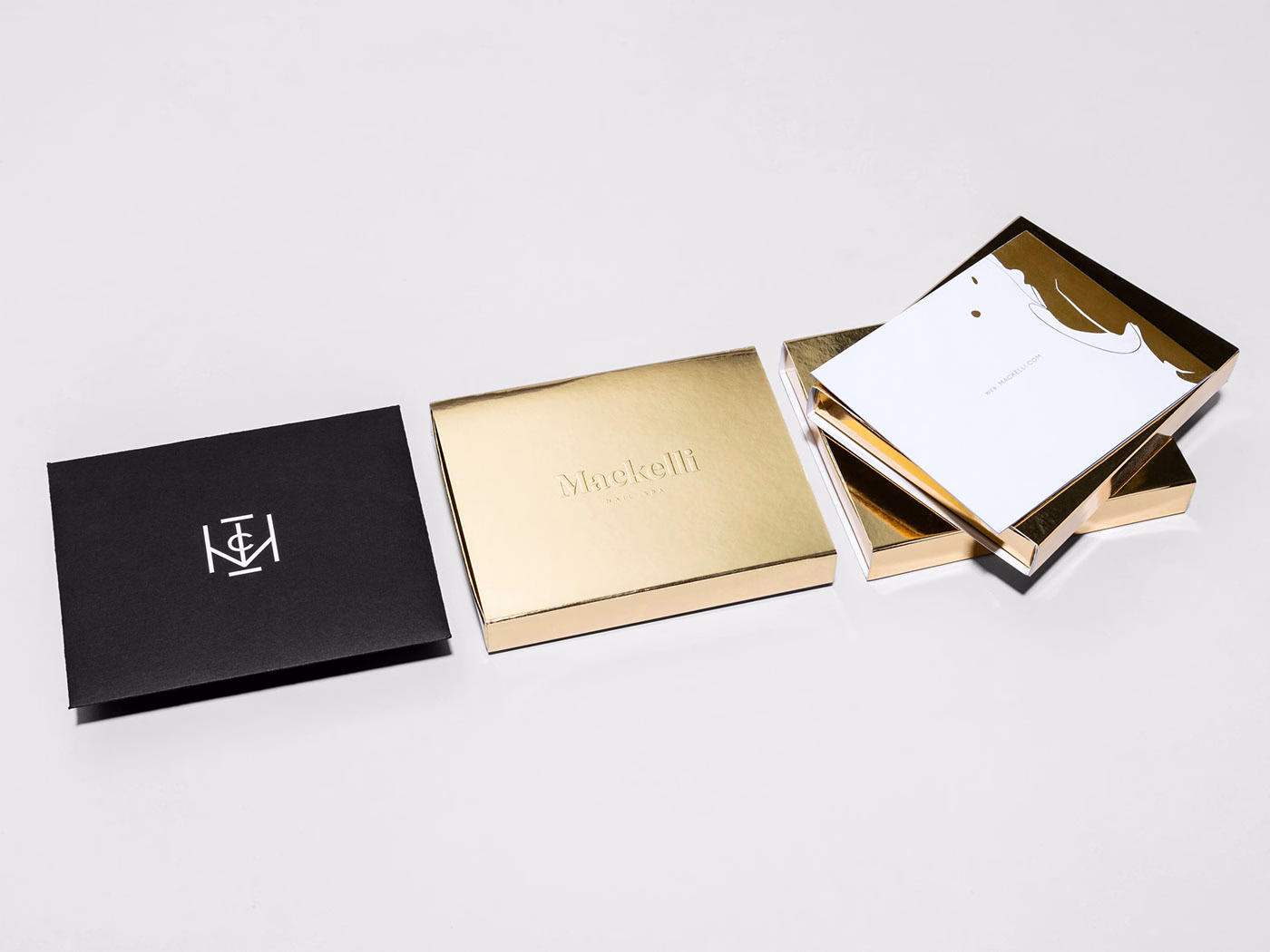 A black envelope with a white logo sits beside three golden boxes, showcasing elegant stationery inside.