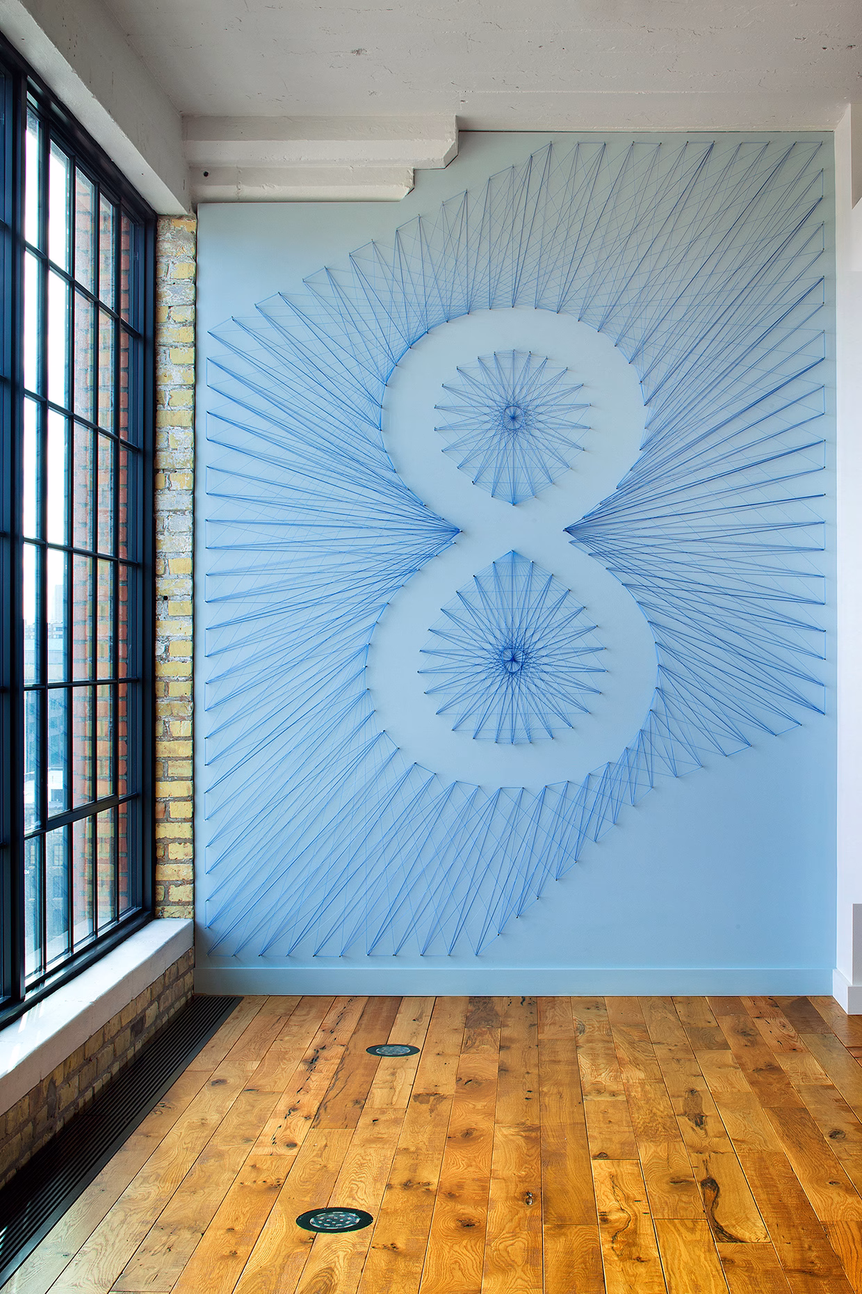 A wall features a blue string art design resembling an "8", set against a light blue background and wooden floor.