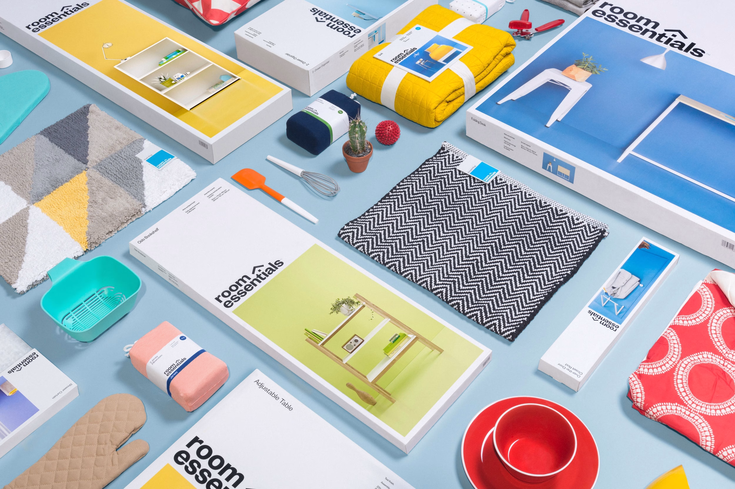 A flat lay displays various home essentials, featuring a yellow blanket and a patterned rug among colorful packaging.