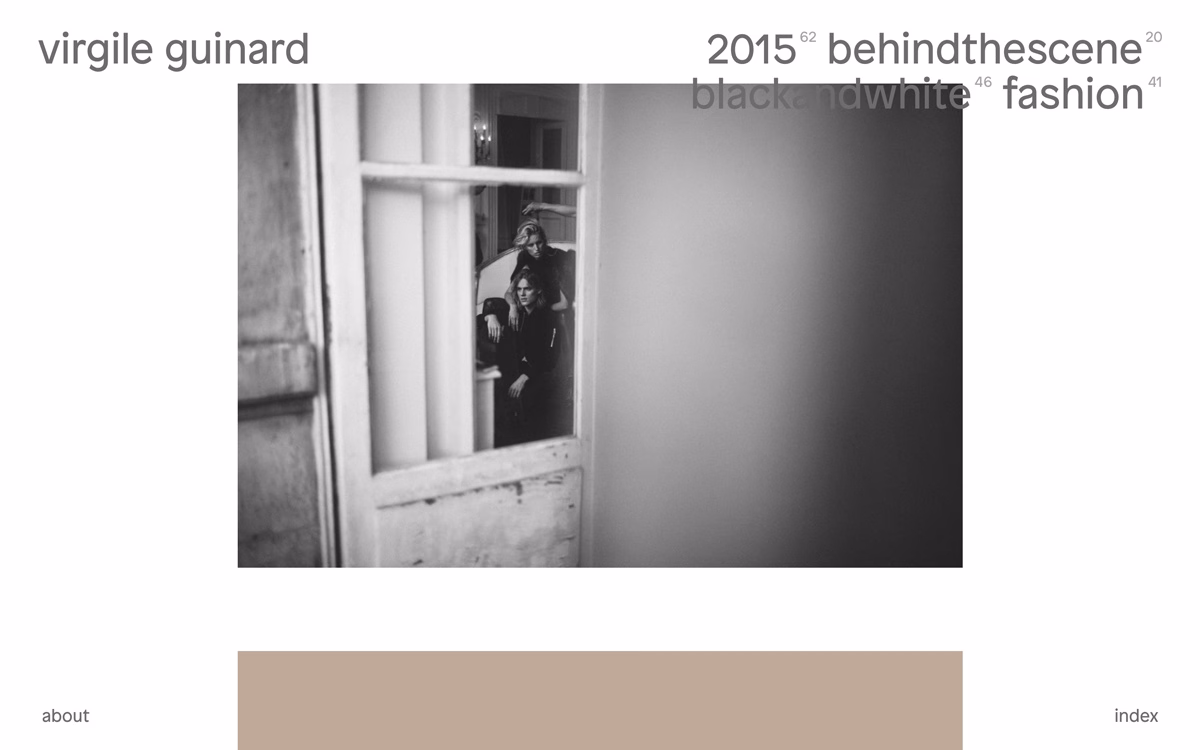 A black and white photo shows two models, partially framed by a doorway, with a textured wall in the background.