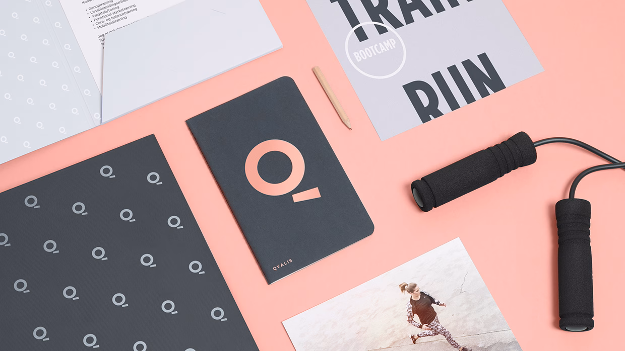 A layout of fitness materials on a peach background, featuring a dark notebook with a logo and a jump rope.