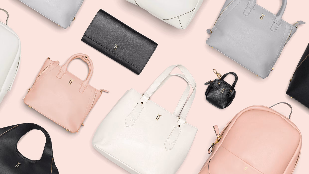An arrangement of various handbags in white, pink, gray, and black leather on a soft pink background.