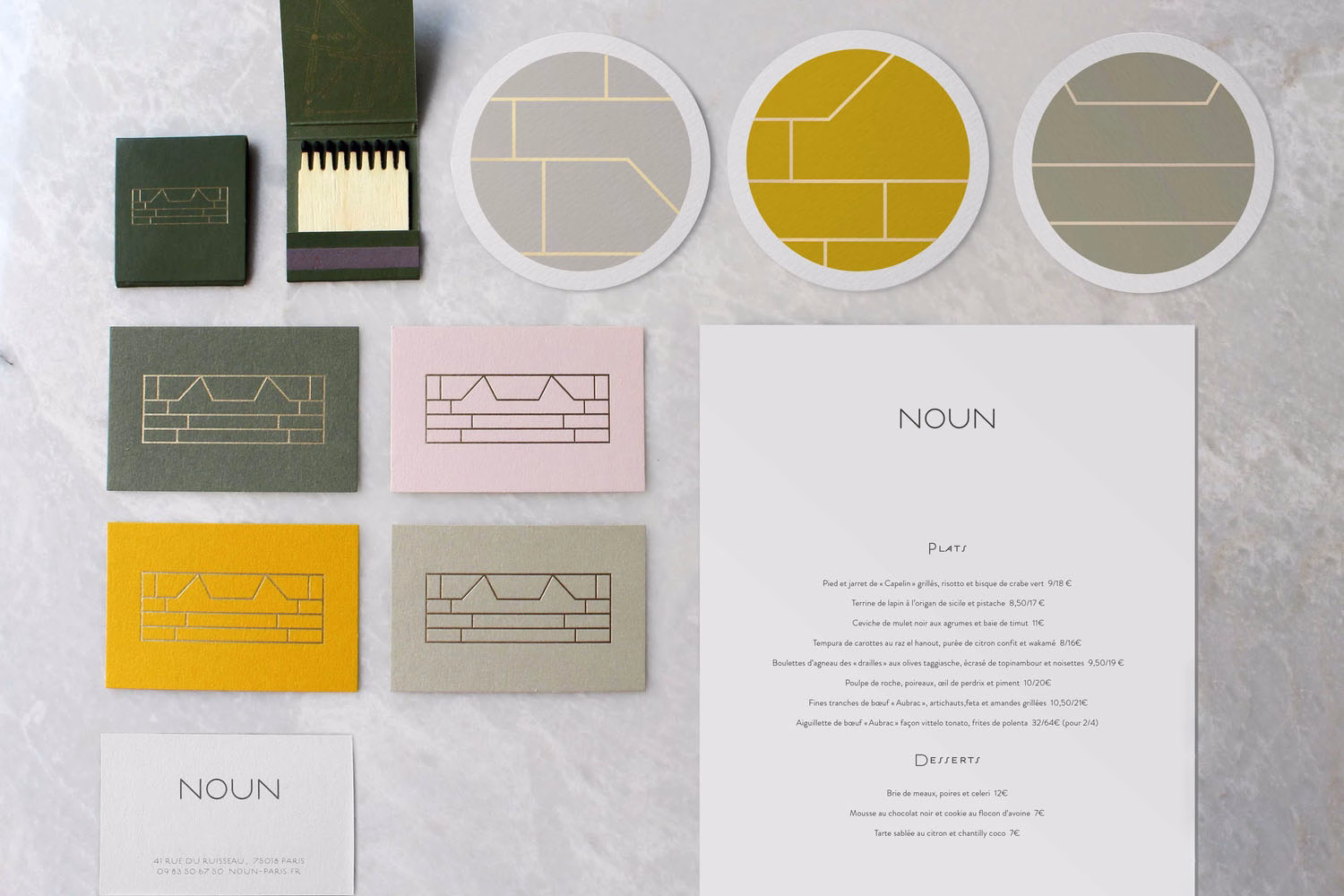 A collection of business cards and a menu with geometric designs in calming colors on a marble surface.