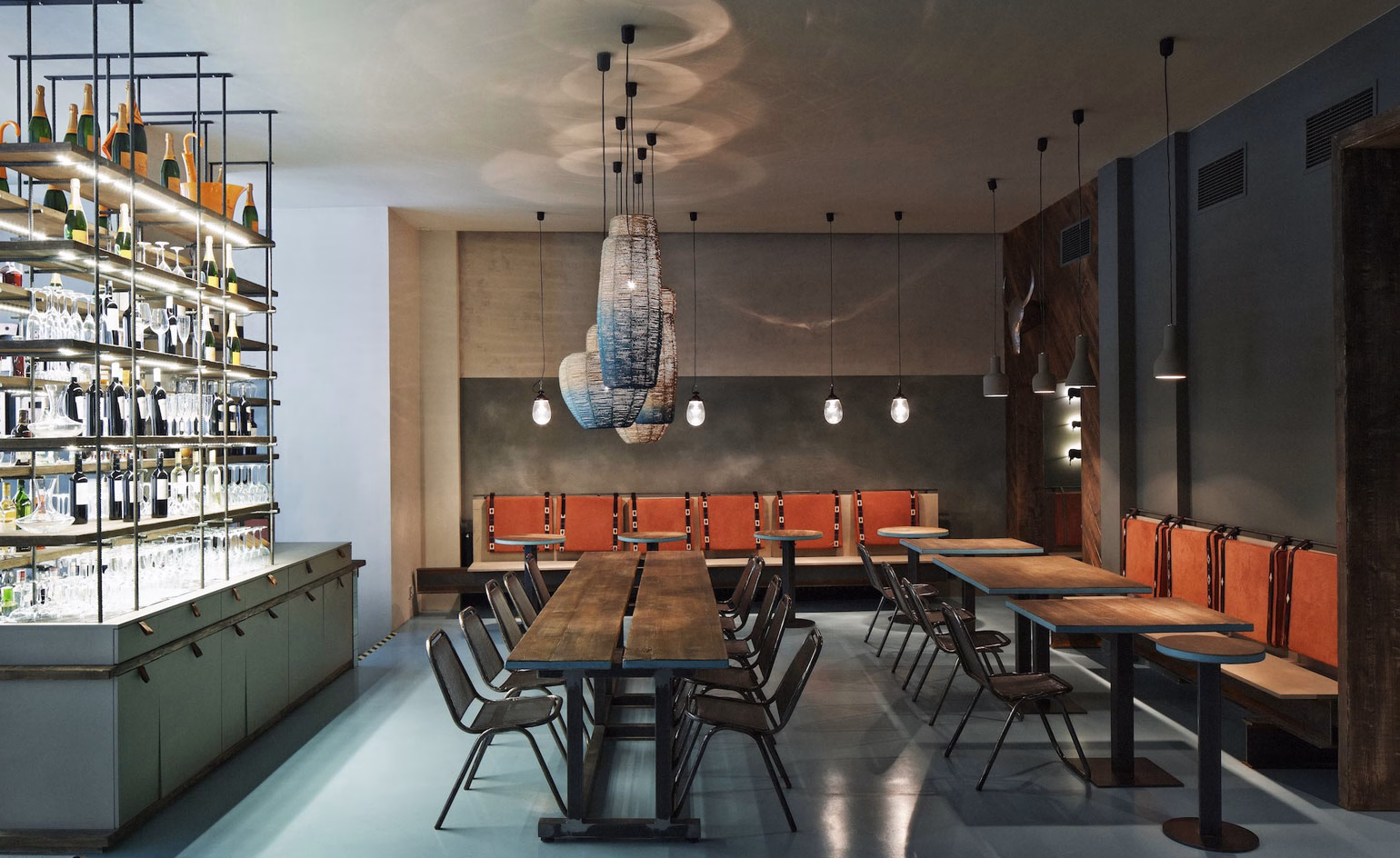 A modern restaurant interior features wooden tables, terracotta accents, and soft lighting from hanging fixtures.