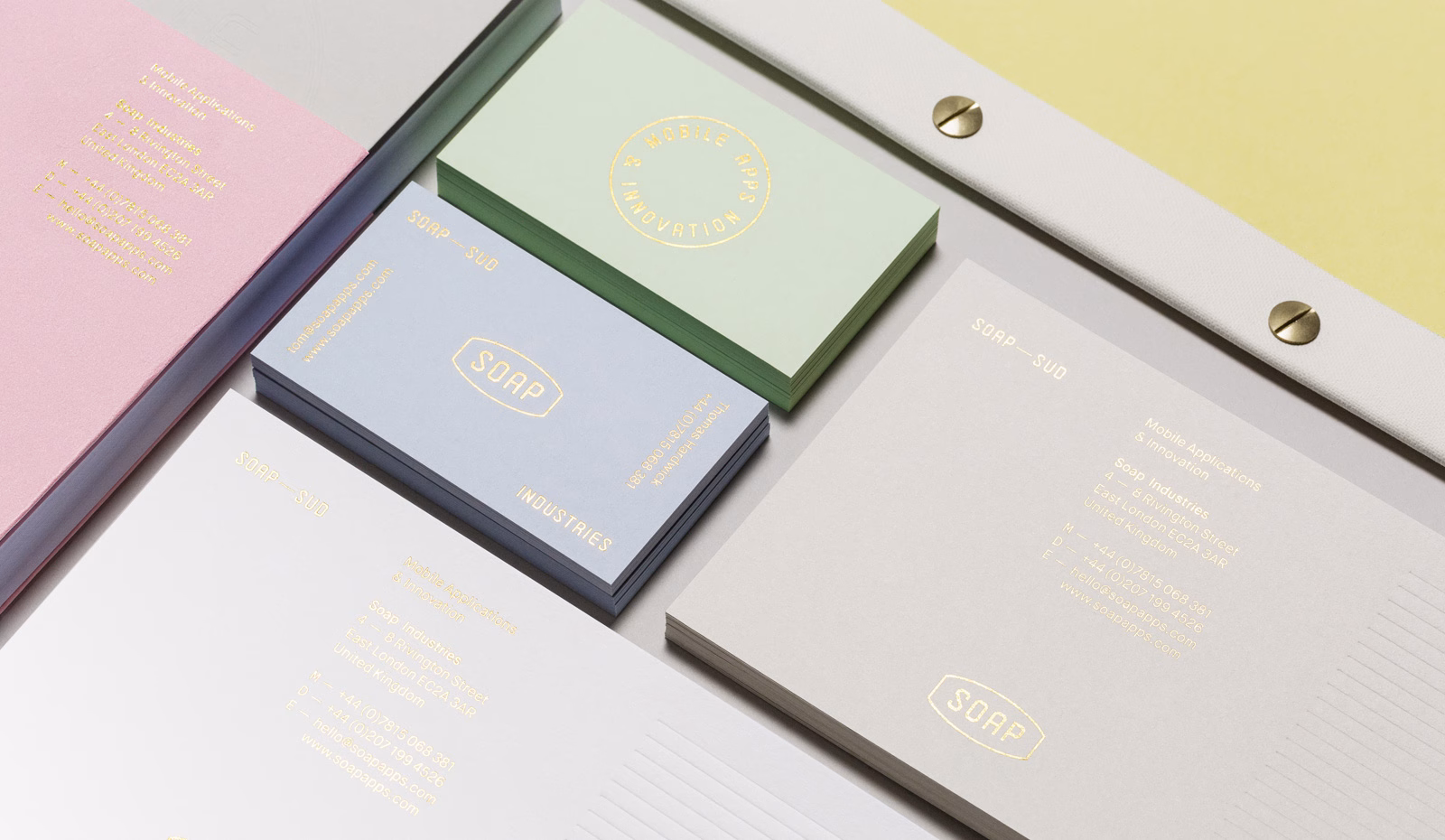 A collection of business cards and stationary in pastel colors, featuring gold typography on a textured surface.