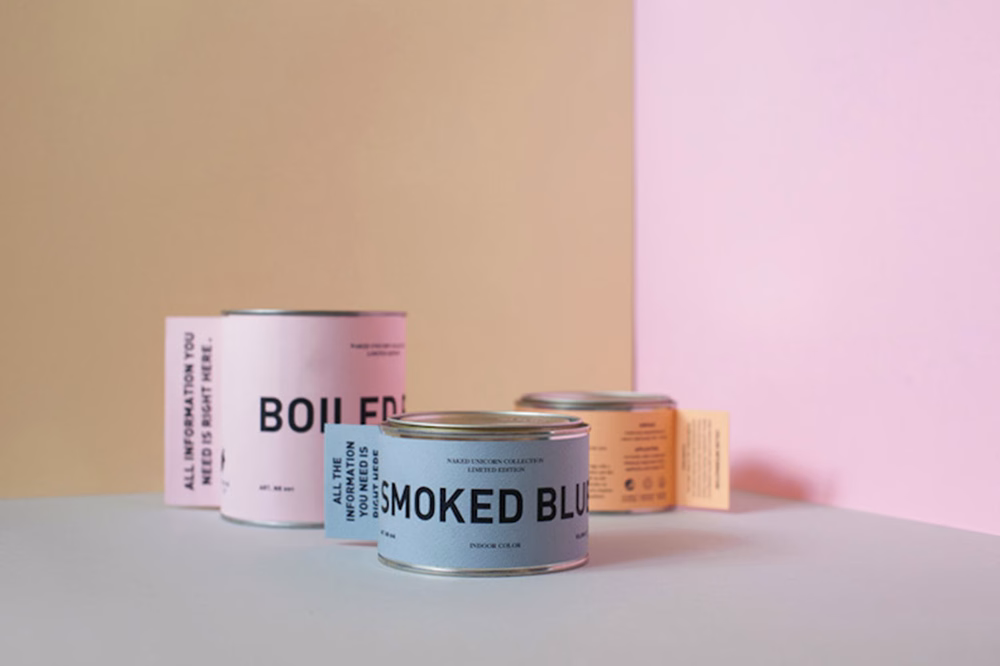 Three paint cans with bold typographic labels in pastel pink and blue, arranged against a soft, neutral background.