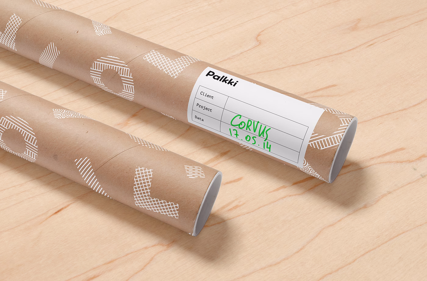 Two cardboard tubes with white geometric patterns are placed on a light wood surface, one labeled with project details.