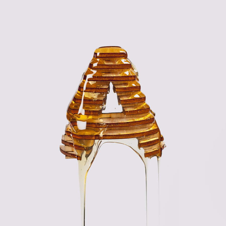 A layered, amber-colored letter "A" drips with golden syrup against a light gray background.