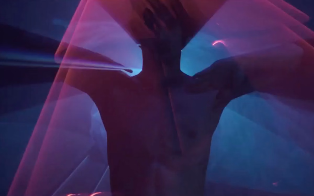 A figure is partially obscured by vibrant layers of light in pink and blue hues, creating a dynamic, abstract composition.