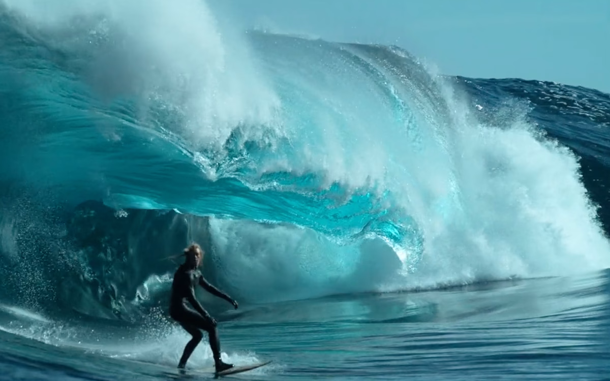 A surfer rides a wave, framed by the towering blue and frothy white crest of the ocean.