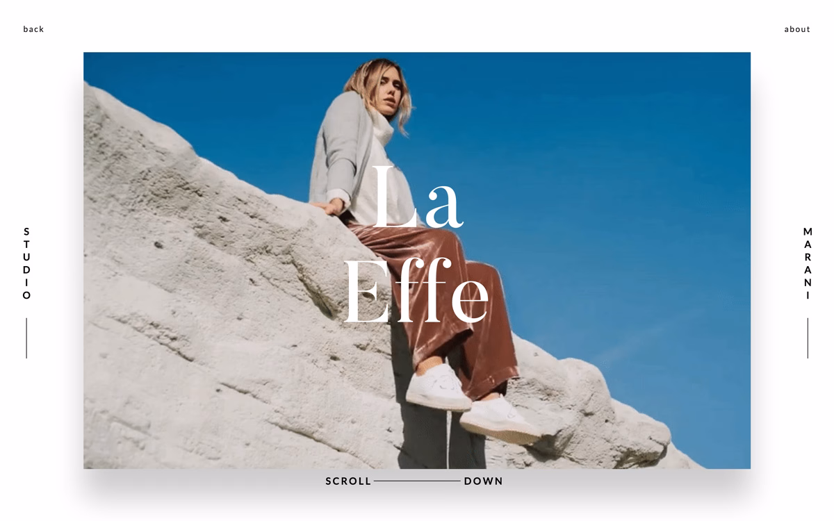 A woman in a cozy sweater and shiny brown pants sits casually on a light stone surface under a clear blue sky.