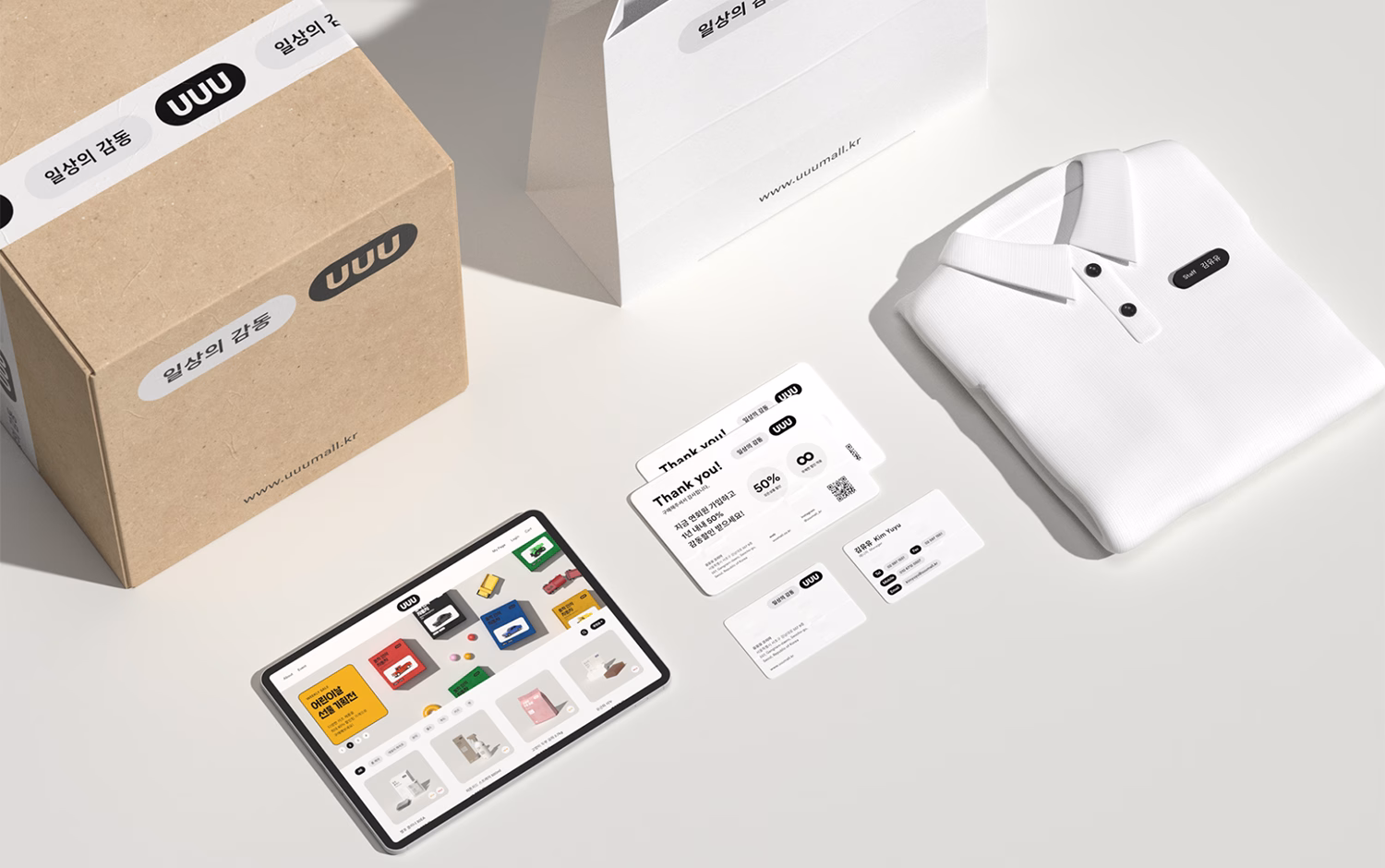 A flat lay of a brown box, a white garment, a tablet displaying colorful products, and various business cards.